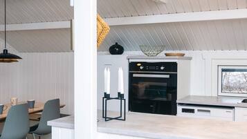 A modern kitchen with a built-in oven, a dining area with chairs, and a large window.