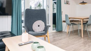 Ein modernes Wohnzimmer mit einem grauen Sessel, einem Holztisch und einem an der Wand befestigten Fernseher.