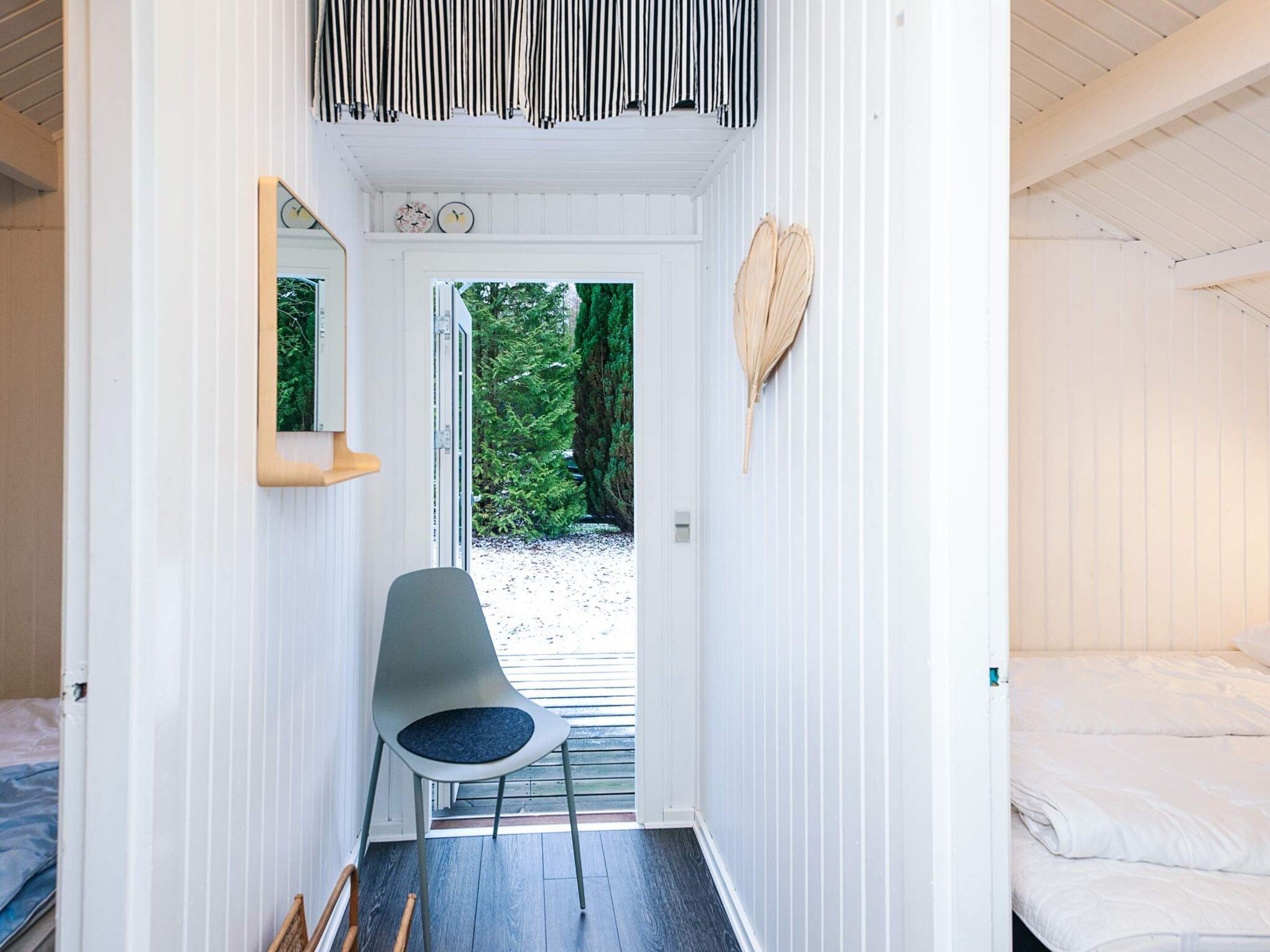 A narrow hallway with a chair, a bed, and a view of greenery outside.