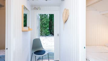 A narrow hallway with a chair, a bed, and a view of greenery outside.