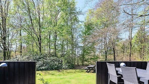 Eine Holzterrasse mit Tisch und Stühlen, umgeben von einem Holzzaun, mit Blick auf eine Rasenfläche mit Bäumen.