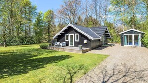 Eine Hütte mit einer Terrasse, einer kleinen Veranda und einer Auffahrt mit Kies.