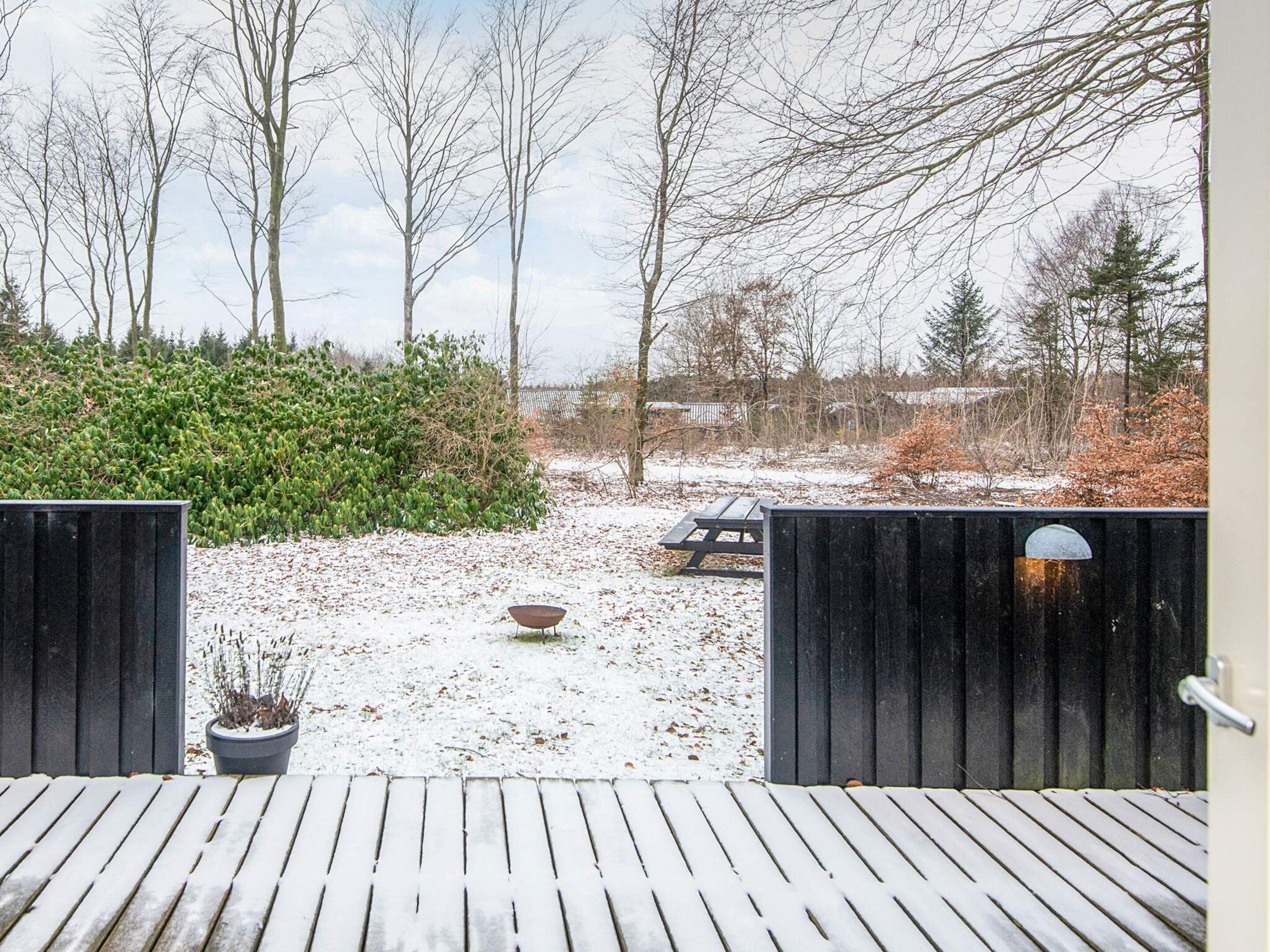 A wooden deck leading to a snowy garden with a bench and a potted plant.