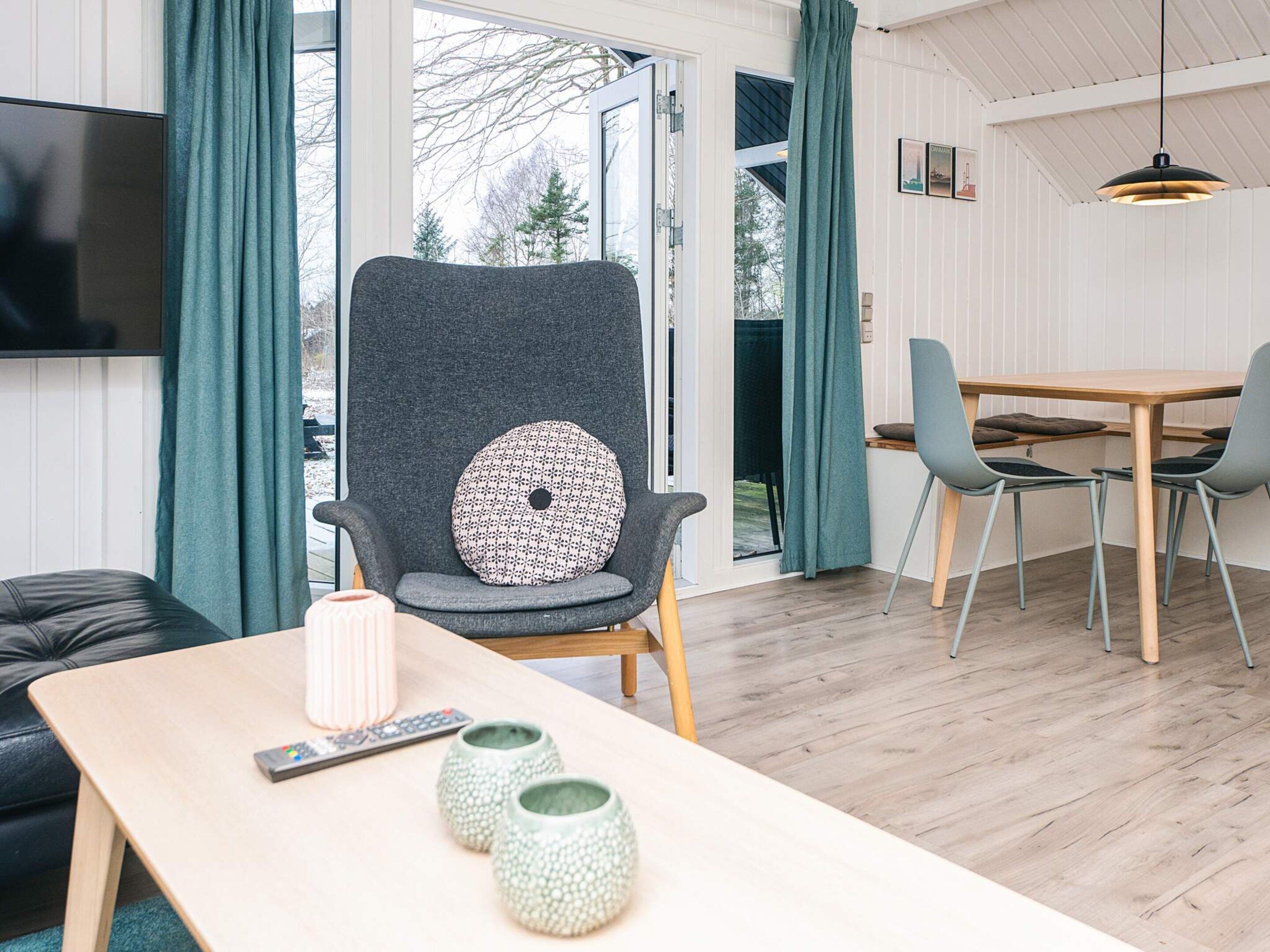 A modern living room with a grey armchair, a wooden table, and a TV mounted on the wall.
