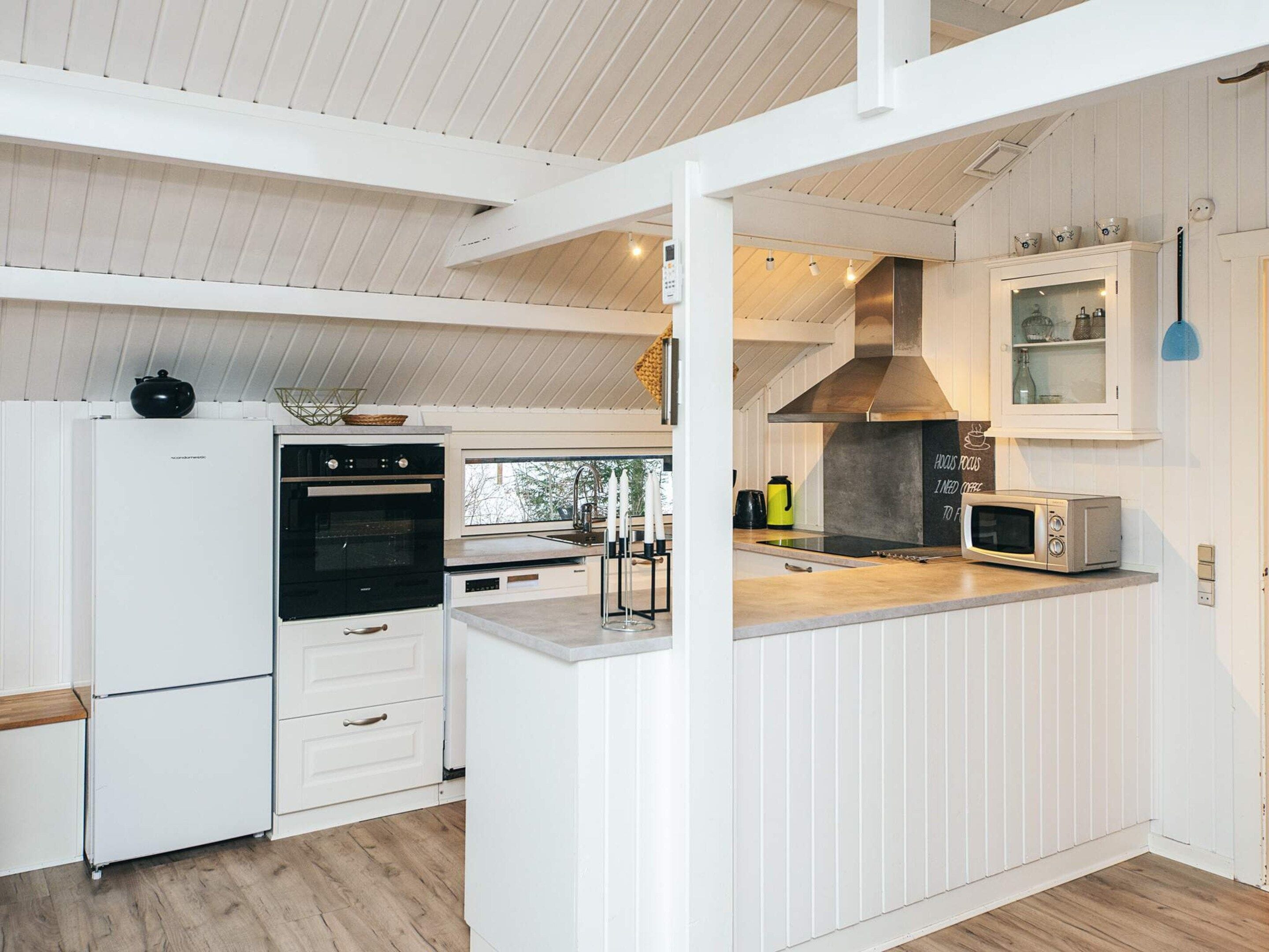 A modern kitchen with white cabinetry, a built-in oven, a microwave, and a large window providing natural light.