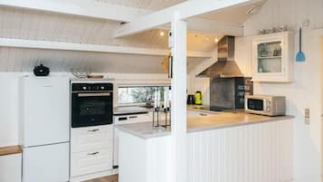 A modern kitchen with white cabinetry, a built-in oven, a microwave, and a large window providing natural light.