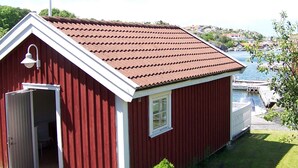 A red wooden building with a white door and window, situated near a body of water with boats. - 4 Person Holiday Home in Ronnang (Roennaeng)