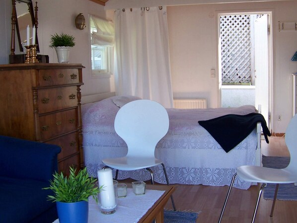 A bedroom with a bed, two white chairs, a dresser, a mirror, a window with curtains, and a potted plant. - 4 Person Holiday Home in Ronnang (Roennaeng)