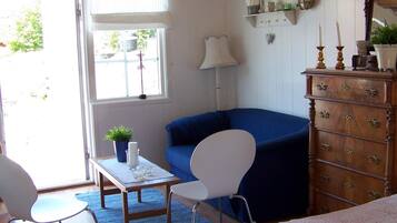 Una habitación con un sillón azul, un aparador de madera, una mesita con una planta y una ventana con persianas.