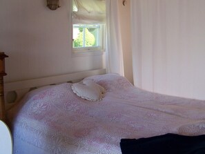 A bed with a white knitted blanket and pillows, a wooden headboard, and a window with curtains. - 4 Person Holiday Home in Ronnang (Roennaeng)