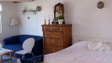 A room with a bed, a blue sofa, a white chair, a wooden dresser, and a lamp.