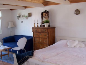 A room with a bed, a blue sofa, a wooden dresser, a white chair, and a lamp. - 4 Person Holiday Home in Ronnang (Roennaeng)