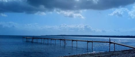 A pier extending into calm waters under a cloudy sky.