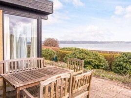 A wooden table and chairs outside a building with a view of a body of water and distant land.