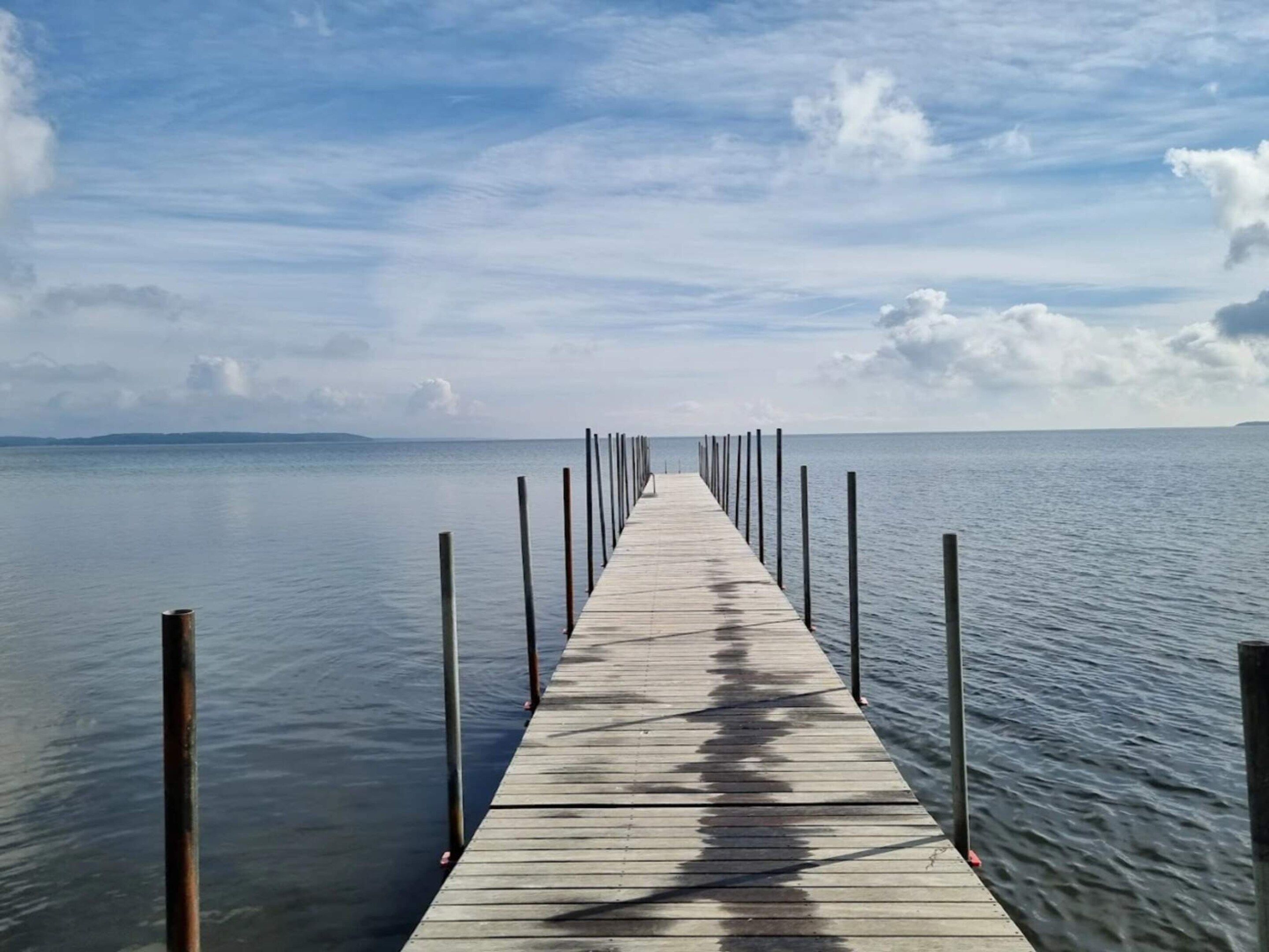 A wooden pier extending into calm water with a clear sky above.