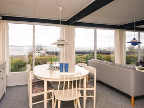 Una habitación con una mesa redonda, sillas, un sofá y ventanas amplias que dan al mar.