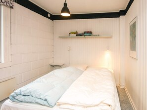 Una habitación con una cama, una estantería con libros, un radiador y una lámpara colgante.
