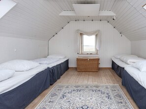 Une chambre avec deux lits, un plancher en bois, un tapis à motifs et une fenêtre avec des rideaux.