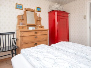 A bedroom with a bed, a wooden dresser, a red wardrobe, and a chair. - 6 Person Holiday Home in Harboore (Harboore)