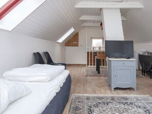 Une chambre à coucher avec un lit, deux chaises, un téléviseur posé sur un meuble et un plancher en bois.