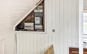 Una habitación con techo inclinado, panel eléctrico empotrado y suelo de madera.