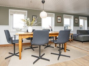 Un coin repas avec une table en bois et des chaises grises, un vase rempli de fleurs et un luminaire suspendu.