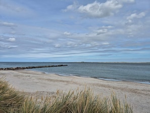 Une plage dotée d’une digue rocheuse, d’un rivage sablonneux et de dunes herbeuses.