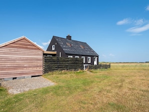 Une maison à deux étages, avec un toit en pente et une clôture en bois à l’avant.