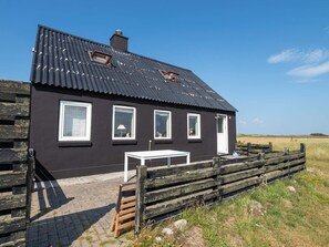 A black house with a metal roof, white windows, and a small table outside.