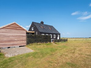 A two-story house with a sloped roof, a wooden fence, and a gravel driveway. - 6 Person Holiday Home in Harboore (Harboore)