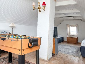 A room with a foosball table, a desk with a computer, a window with a view, and a bed.