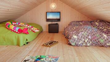 A cozy attic bedroom with a sloped ceiling, a flat-screen TV mounted on the wall, a green and a patterned bed, and a small chest of drawers.