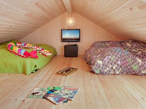 A cozy attic bedroom with a sloped ceiling, a flat-screen TV mounted on the wall, a green and a patterned bed, and a small chest of drawers. - 4 Star Holiday Home in Tranekaer (Tranekaer)