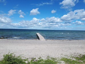 A beach with a concrete pier extending into the water, a clear sky, and a distant shoreline. - 4 Star Holiday Home in Tranekaer (Tranekaer)