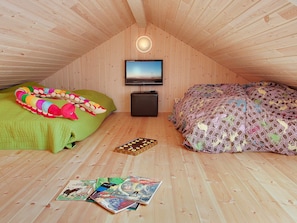 A cozy attic bedroom with a sloped ceiling, a television mounted on the wall, and a bed with patterned bedding.