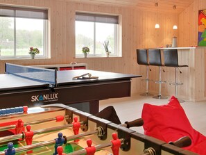 A room with a foosball table, a ping pong table, and two bar stools.