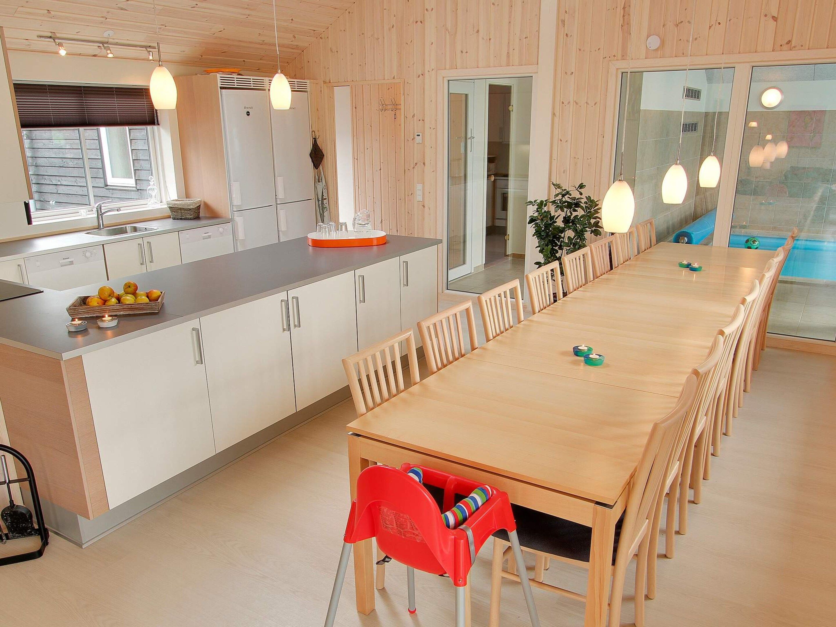 Una cocina moderna con una isla de madera, un comedor con una mesa larga y sillas, y vista al exterior.