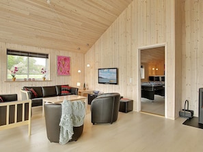 Sala de estar moderna com teto de madeira, sofá, televisão e vista para o exterior através de uma janela.