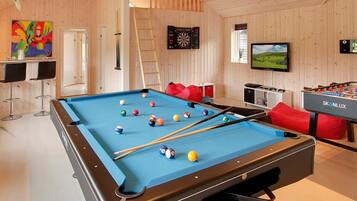 A pool table with balls, a foosball table, a dartboard, and a television.
