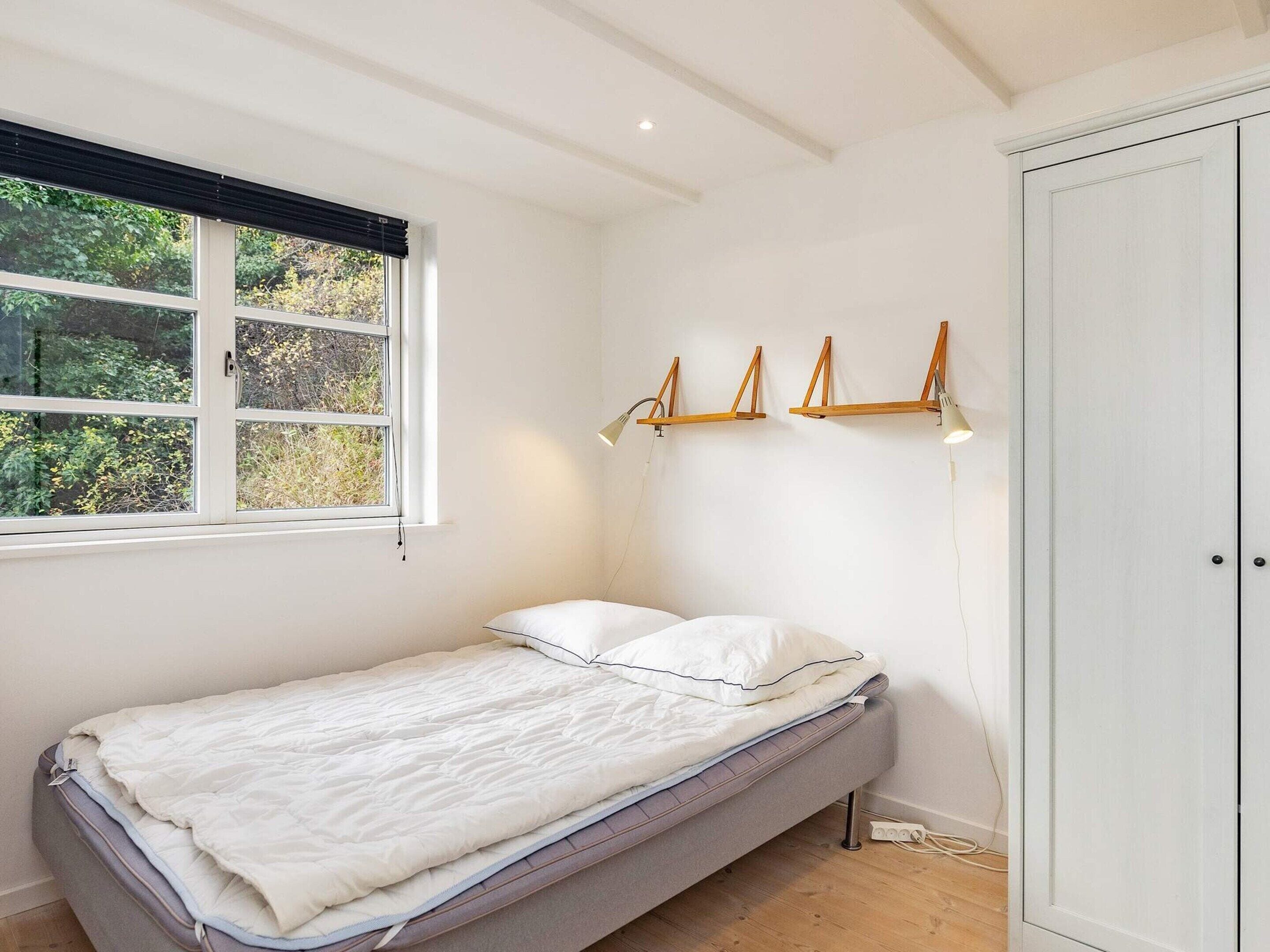 A small, single-bed room with a window, a wardrobe, and wall-mounted lamps.