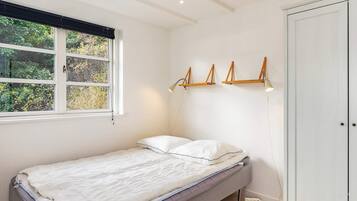 A small, single-bed room with a window, a wardrobe, and wall-mounted lamps.