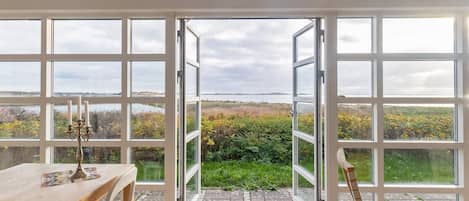 A room with a large sliding glass door leading to an outdoor area with a view of a body of water and vegetation.