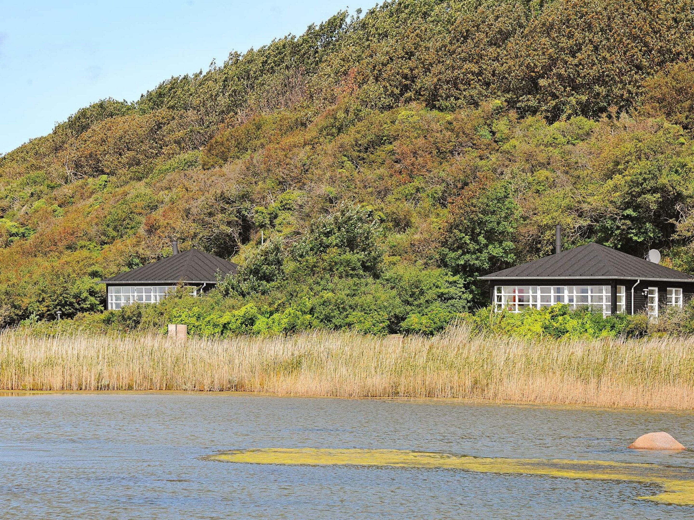 Two cabins with a lake and forested hill in the background.