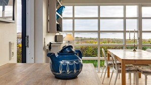 A room with a large window, a table with a blue ceramic pot, and a view of the outdoors.