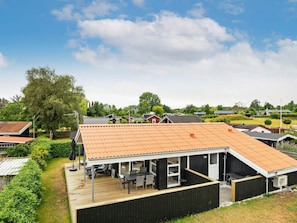 A modern building with a flat roof, a covered outdoor area with seating, and a view of a residential area in the background.