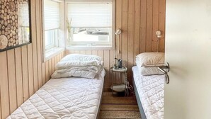 A small, cozy room with two single beds, a window with blinds, a small table with a lamp, and a mirror on the wall. - 6 Person Holiday Home in Tranekaer-by Traum (Tranekaer)