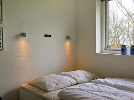 A bedroom with a single bed, two wall-mounted light fixtures, a window with a view of trees, and a small shelf with containers.