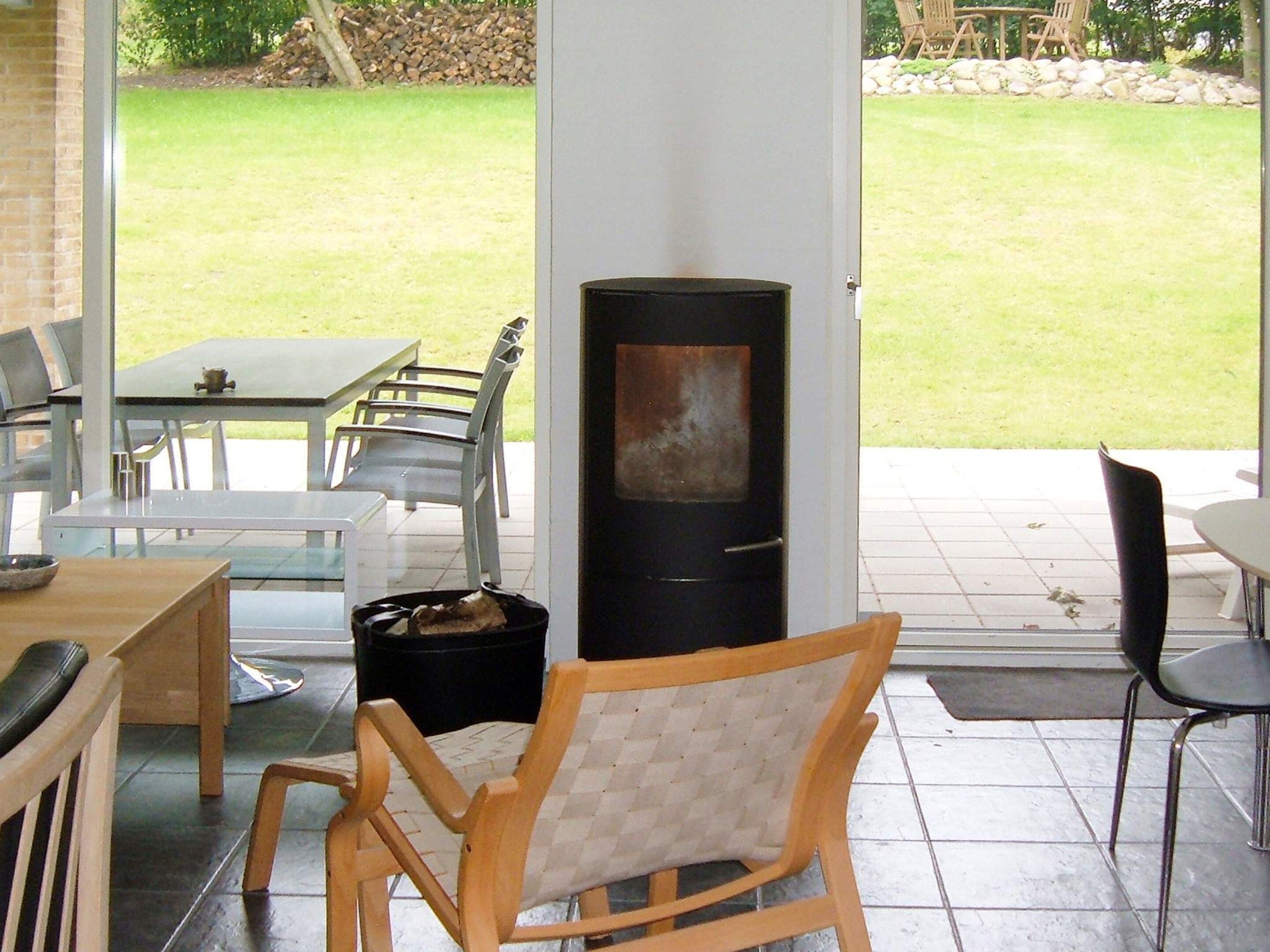 An outdoor patio with a table and chairs, a wood-burning stove, and a view of a grassy area.