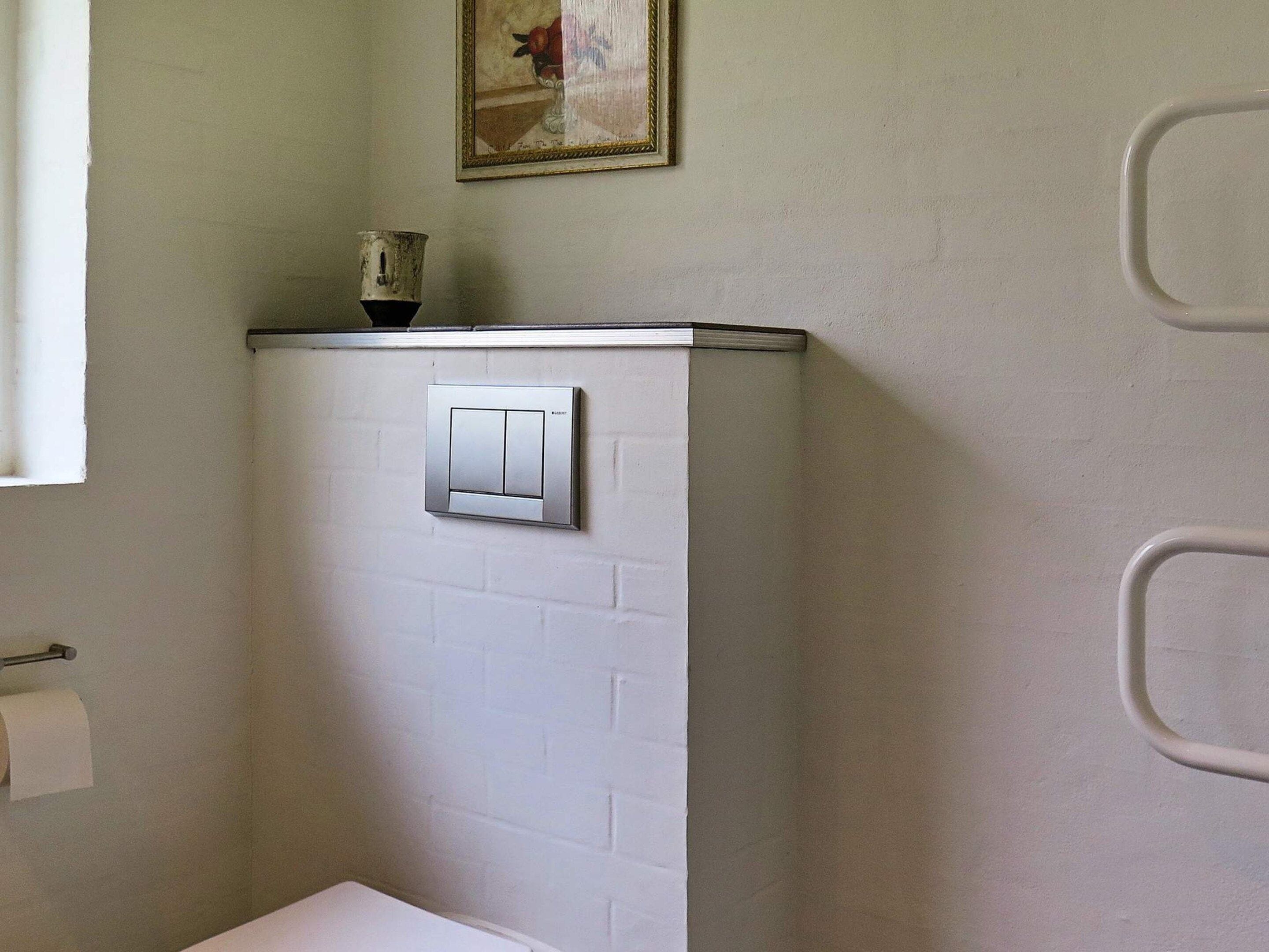 A bathroom with a white brick wall, a light switch, a towel dispenser, and a framed picture above the switch.