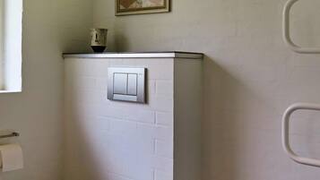 A bathroom with a white brick wall, a light switch, a towel dispenser, and a framed picture above the switch.